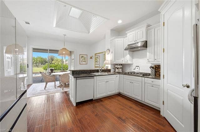 1936 Empress Ct, Naples, FL 34110 Kitchen featuring white cabinetry, propane gas stovetop, dark countertops, wood-finish flooring, and a skylight