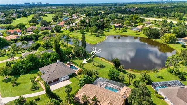 1936 Empress Ct, Naples, FL 34110 Lush green landscape with 0.98 Acre lot featuring a lake view, fenced yard, surrounded by mature trees and residential properties
