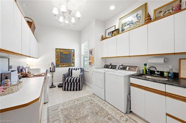 1936 Empress Ct, Naples, FL 34110 White cabinetry, tiled flooring, built-in countertop and desk area, laundry appliances, and a utility sink with a dark countertop