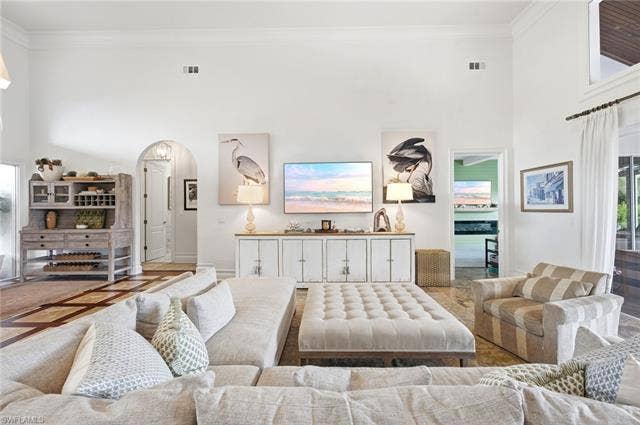 1936 Empress Ct, Naples, FL 34110 Vaulted ceiling with crown molding, arched doorway, built-in media console, wood-finish flooring, and a window with white drapery