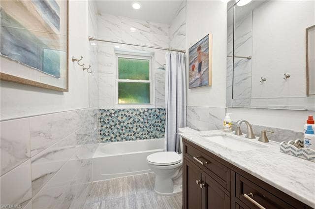 1936 Empress Ct, Naples, FL 34110 Bathroom featuring a single vanity with a white countertop and dark wood-finish cabinetry, a tub with a shower and subway tile surround, mosaic accent tiling, and a window