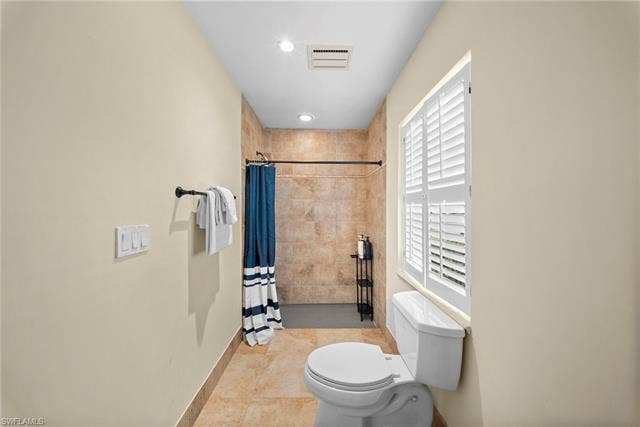 2171 Kings Lake Blvd, Naples, FL 34112 Recessed lighting, tiled shower surround, tiled flooring, window with white plantation shutters, and a white commode