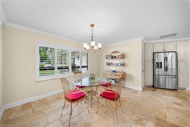 2171 Kings Lake Blvd, Naples, FL 34112 Travertine tile flooring, crown molding, white plantation shutters, built-in cabinetry, and a stainless steel refrigerator