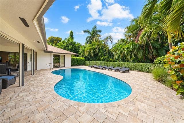 2171 Kings Lake Blvd, Naples, FL 34112 Curved pool with integrated handrail, surrounded by a paver patio and lush tropical landscaping