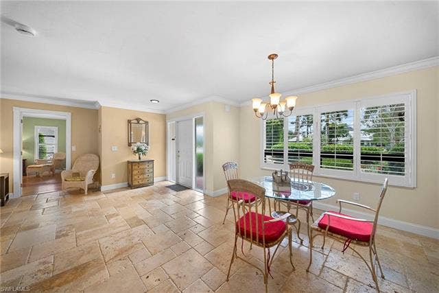 2171 Kings Lake Blvd, Naples, FL 34112 Textured stone flooring, crown molding, white paneled entry door with sidelight, large window with white plantation shutters, and a chandelier with glass shades