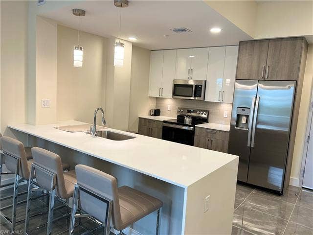 26600 Rosewood Pointe Dr, #B-107, Bonita Springs, FL 34135 Kitchen with sink, appliances with stainless steel finishes, white cabinetry, a kitchen bar, and dark brown cabinetry