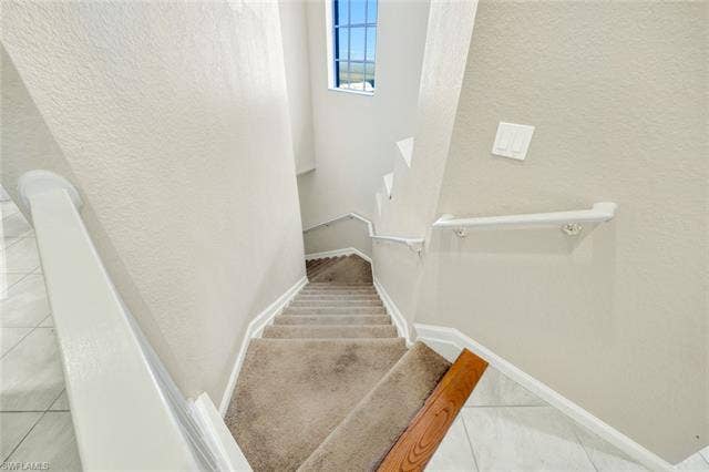 10060 Valiant Ct, #202, Miromar Lakes, FL 33913 Multi-level staircase featuring carpeted treads, white painted handrails, and textured wall finishes