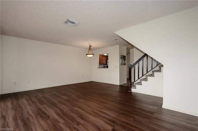 25484 Cockleshell Dr, #901, Bonita Springs, FL 34135 Unfurnished living room with dark wood-style flooring, stairs, and a textured ceiling