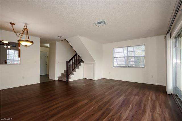 25484 Cockleshell Dr, #901, Bonita Springs, FL 34135 Unfurnished living room with a textured ceiling, dark wood-type flooring, stairs, and a ceiling fan
