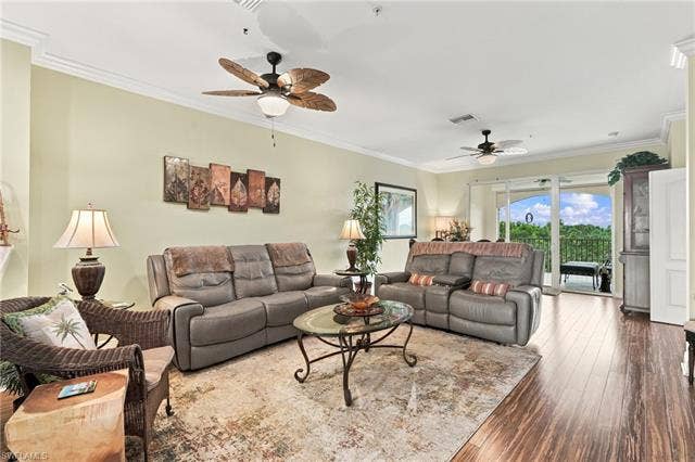 11041 Gulf Reflections Dr, #403, Fort Myers, FL 33908 Spacious living area featuring crown molding, two ceiling fans with integrated lighting, wood-finish flooring, and sliding glass doors leading to a balcony