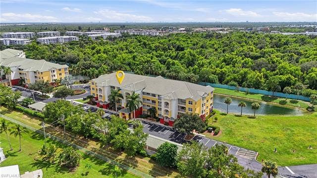 11041 Gulf Reflections Dr, #403, Fort Myers, FL 33908 Multi-story building featuring a yellow and red exterior, multiple balconies, a surrounding paved parking area, and an adjacent water feature with lush landscaping