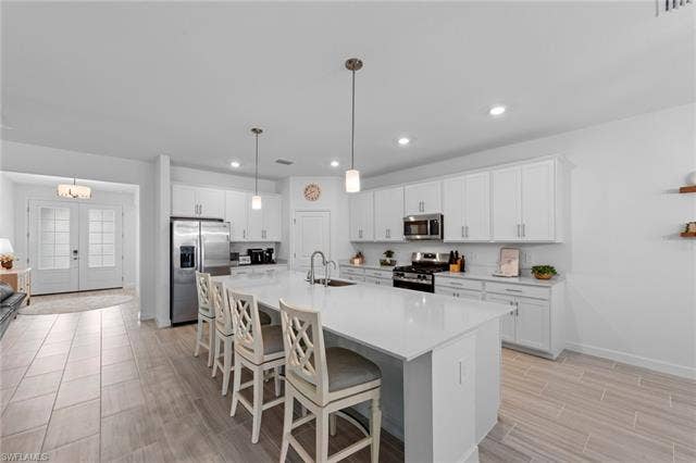 44810 Marina Ln, Punta Gorda, FL 33982 Spacious kitchen featuring white cabinetry, a large center island, stainless steel appliances, pendant lighting, and wood-finish tile flooring