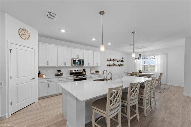 44810 Marina Ln, Punta Gorda, FL 33982 Open-concept kitchen featuring white cabinetry, stainless steel appliances, a large center island with counter seating, and wood-finish flooring