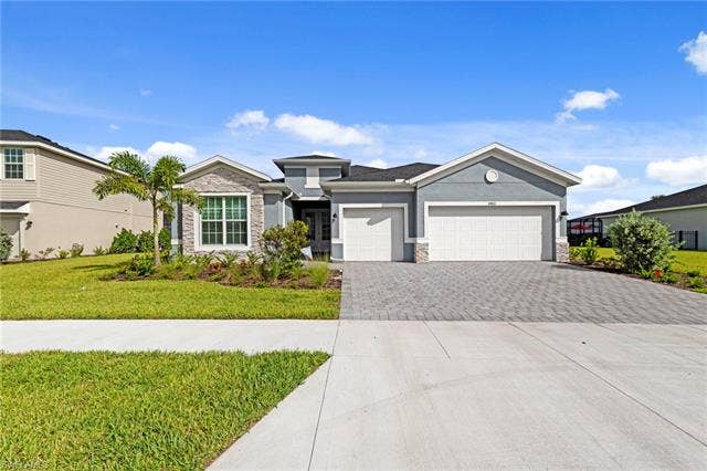 44810 Marina Ln, Punta Gorda, FL 33982 Contemporary residence featuring a stucco and stone facade, a paver driveway, an attached multi-car garage, and a manicured front lawn with mature landscaping
