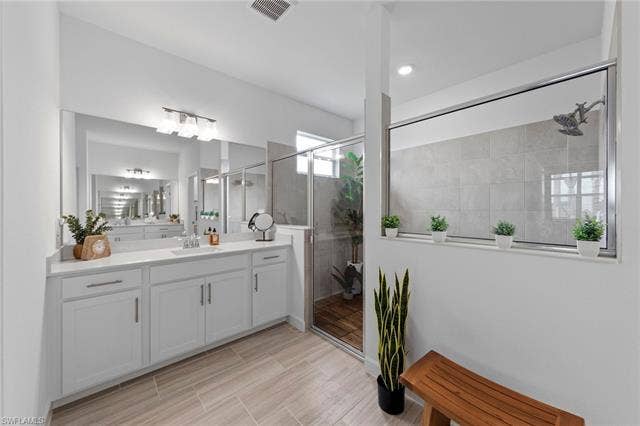 44810 Marina Ln, Punta Gorda, FL 33982 Dual basin vanity with white cabinetry and chrome hardware, a large wall-mounted mirror, wood-finish tile flooring, and a walk-in shower with a glass enclosure and tiled walls