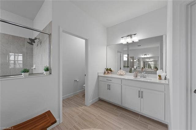 44810 Marina Ln, Punta Gorda, FL 33982 Spacious bathroom featuring a glass-enclosed shower, dual vanity with a large mirror, light wood-finish flooring, and a separate water closet
