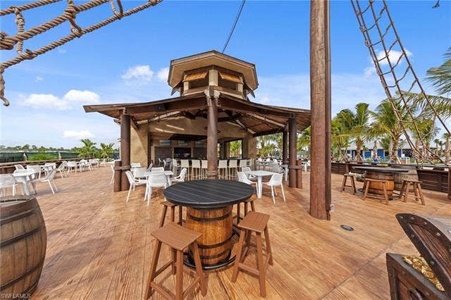 44810 Marina Ln, Punta Gorda, FL 33982 Expansive outdoor deck with wood-finish flooring, featuring a central bar structure with a covered patio, various seating arrangements, and palm trees