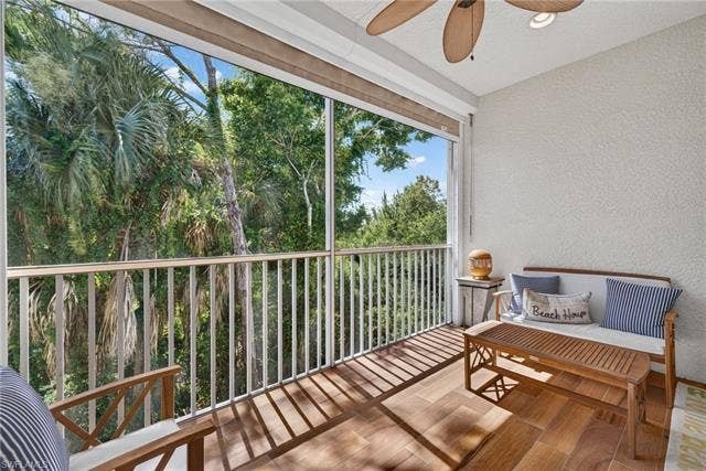 14543 Abaco Lakes Dr, #202, Fort Myers, FL 33908 Lanai view highlighting the spacious outdoor seating area, tropical leaf fan, and serene, private green backdrop.