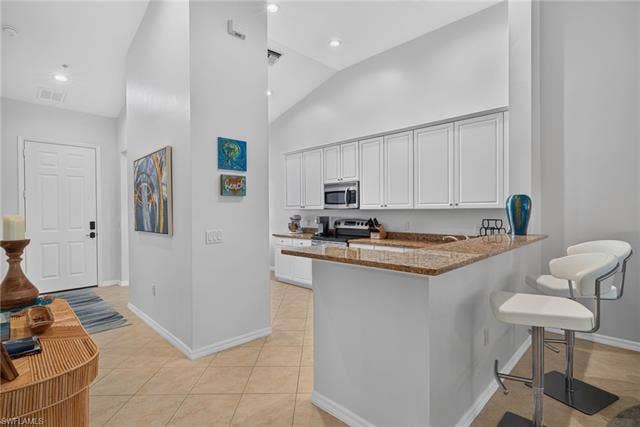 14543 Abaco Lakes Dr, #202, Fort Myers, FL 33908 Modern open kitchen featuring bright white cabinetry, premium granite countertops, soaring vaulted ceilings, and a convenient breakfast bar