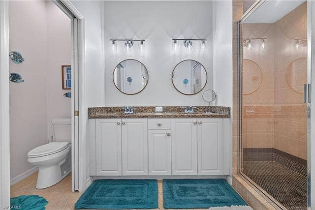 14543 Abaco Lakes Dr, #202, Fort Myers, FL 33908 En suite primary bathroom featuring a dual-sink vanity, modern round mirrors, bright vanity lighting, a private water closet, and a glass-enclosed walk-in shower.
