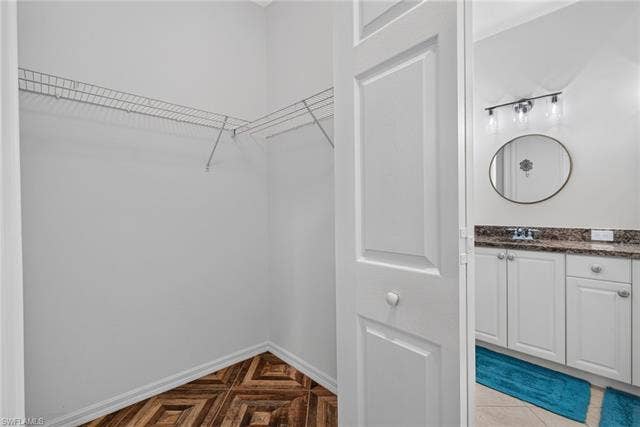 14543 Abaco Lakes Dr, #202, Fort Myers, FL 33908 Spacious primary walk-in closet featuring built-in wire shelving, matching herringbone floors, and direct access to the en suite bathroom.