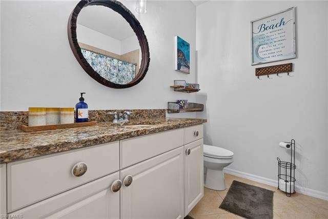 14543 Abaco Lakes Dr, #202, Fort Myers, FL 33908 Well-appointed guest bathroom complete with a granite-topped vanity, a large round statement mirror, modern lighting, and a neutral tile floor.