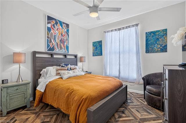 14543 Abaco Lakes Dr, #202, Fort Myers, FL 33908 Cozy second bedroom featuring continuous herringbone flooring, dynamic artwork, a modern ceiling fan, and plenty of space for guests.
