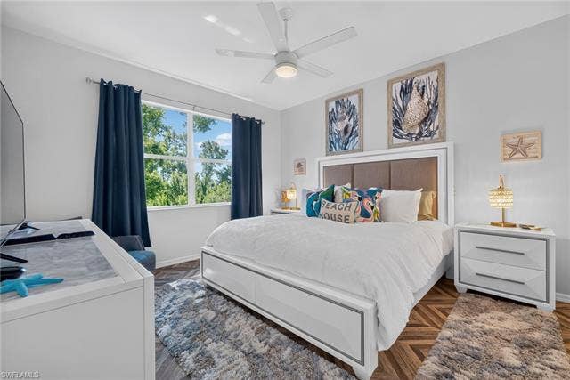 14543 Abaco Lakes Dr, #202, Fort Myers, FL 33908 Serene primary bedroom offering a spacious layout, stylish herringbone flooring, a modern ceiling fan, and peaceful tree-lined views.