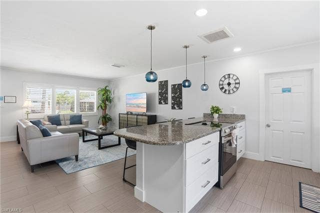 240 Fairweather Ln, Fort Myers Beach, FL 33931 Open-concept living space featuring a kitchen island with granite countertops, stainless steel appliances, and pendant lighting - Virtually Edited Image