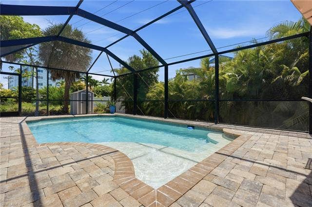 240 Fairweather Ln, Fort Myers Beach, FL 33931 Screened-in pool area featuring a rectangular pool with an integrated sun shelf, surrounded by a paver patio - Virtually Edited Image