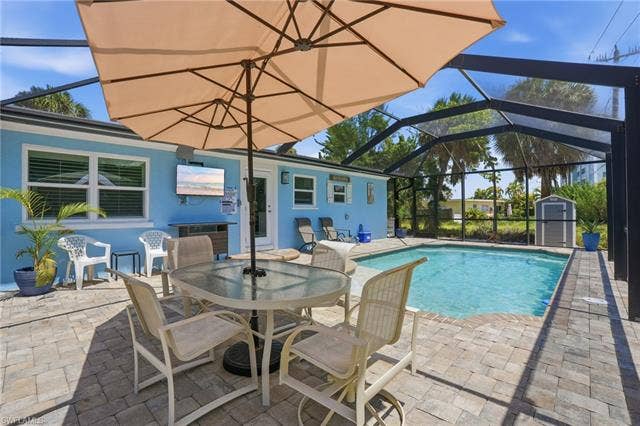 240 Fairweather Ln, Fort Myers Beach, FL 33931 Screened-in pool area featuring a paver deck, a rectangular swimming pool, and a light blue stucco exterior - Virtually Edited Image