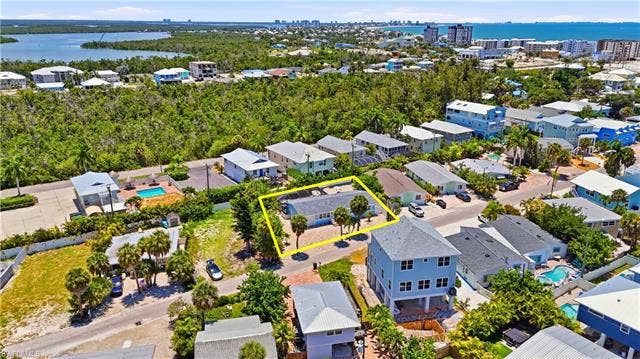240 Fairweather Ln, Fort Myers Beach, FL 33931 Single-story residence set amidst mature trees with a paved driveway and surrounding lush greenery - Virtually Edited Image