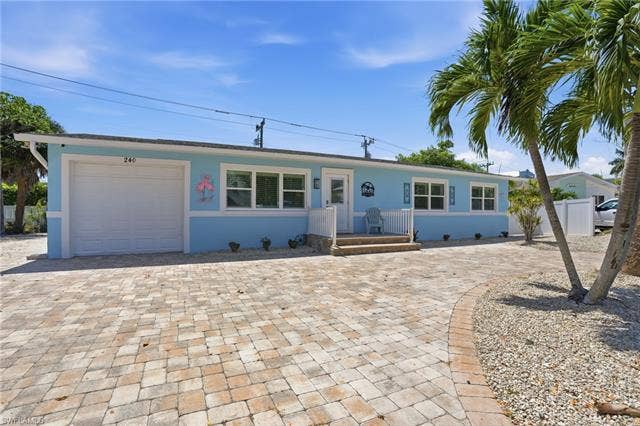 240 Fairweather Ln, Fort Myers Beach, FL 33931 Single-story residence featuring a light blue exterior, white trim, and a paver driveway - Virtually Edited Image