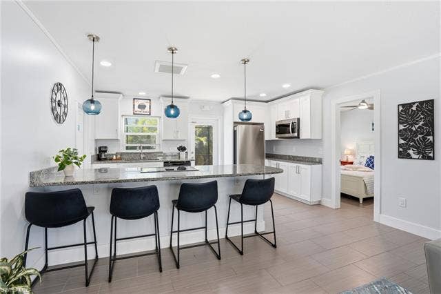 240 Fairweather Ln, Fort Myers Beach, FL 33931 Spacious kitchen featuring an extended peninsula with seating, shaker-style cabinetry, stainless steel appliances, granite countertops, and tile flooring - Virtually Edited Image