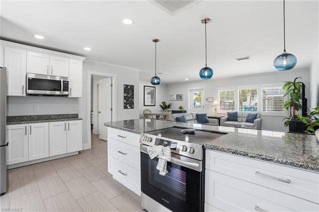 240 Fairweather Ln, Fort Myers Beach, FL 33931 Open-concept kitchen featuring white shaker cabinetry, stainless steel appliances, and a central island with a built-in range - Virtually Edited Image