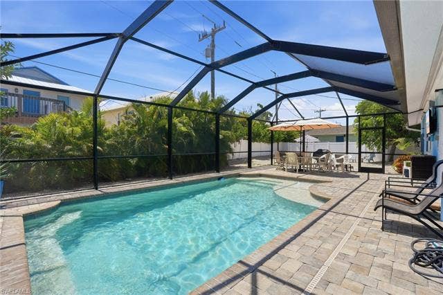240 Fairweather Ln, Fort Myers Beach, FL 33931 Screened swimming pool area with paver decking, integrated sun shelf, and mature perimeter landscaping - Virtually Edited Image