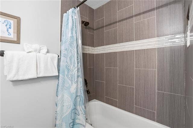 240 Fairweather Ln, Fort Myers Beach, FL 33931 Full bathtub featuring vertically stacked tile walls with a horizontal glass mosaic accent band - Virtually Edited Image