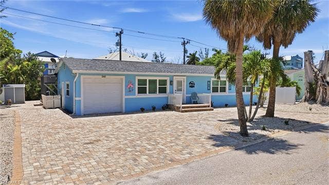 240 Fairweather Ln, Fort Myers Beach, FL 33931 Light blue single-story residence featuring a white garage door and multiple windows - Virtually Edited Image