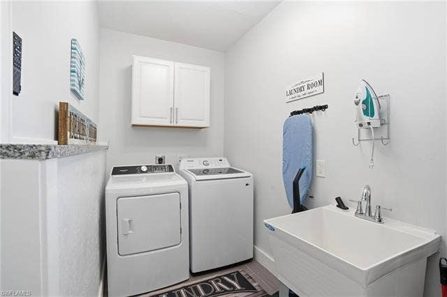 240 Fairweather Ln, Fort Myers Beach, FL 33931 Dedicated laundry area featuring a utility sink with chrome faucet, granite countertop, built-in upper cabinetry, and wood-finish flooring - Virtually Edited Image