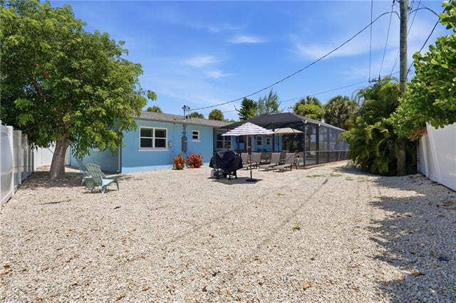 240 Fairweather Ln, Fort Myers Beach, FL 33931 Spacious gravel yard featuring a large mature tree, white privacy fencing, and a screened-in pool enclosure - Virtually Edited Image