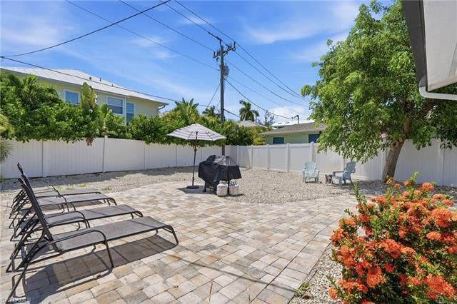 240 Fairweather Ln, Fort Myers Beach, FL 33931 Paved patio area featuring paver stones, a white privacy fence, and mature landscaping - Virtually Edited Image