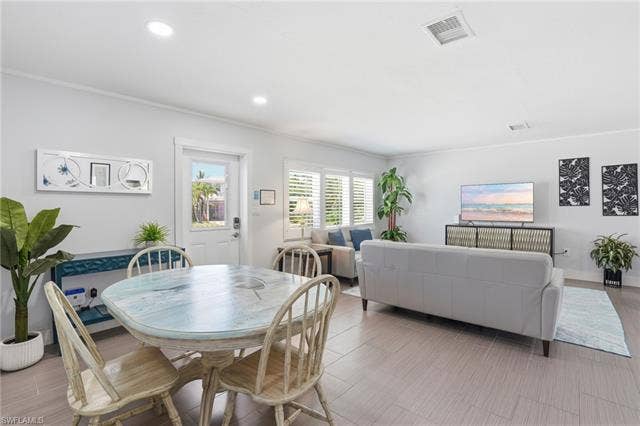 240 Fairweather Ln, Fort Myers Beach, FL 33931 Open-concept living area featuring light-toned tile flooring, recessed lighting, and white plantation shutters - Virtually Edited Image