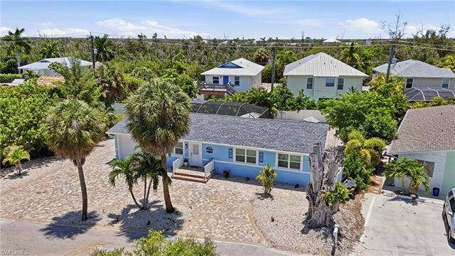 240 Fairweather Ln, Fort Myers Beach, FL 33931 Light blue exterior with white trim, featuring a dark shingle roof and a front porch with white railings - Virtually Edited Image