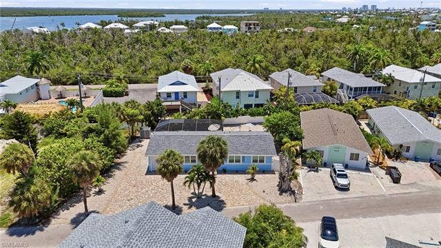 240 Fairweather Ln, Fort Myers Beach, FL 33931 Aerial perspective showcasing a residential area with a prominent light blue single-story home featuring a gray shingle roof and a screened-in pool enclosure - Virtually Edited Image