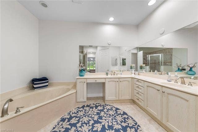 3142 Aviamar Cir, #2104, Naples, FL 34114 Dual vanity with light-toned cabinetry and extensive countertop space, integrated soaking tub with deck-mounted fixtures, large wall-mounted mirrors, and recessed lighting