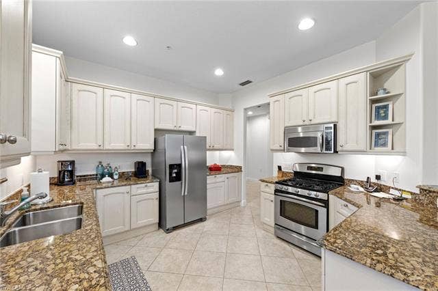3142 Aviamar Cir, #2104, Naples, FL 34114 Spacious kitchen featuring white cabinetry with raised-panel doors, granite countertops, and stainless steel appliances including a French-door refrigerator, gas range, and microwave