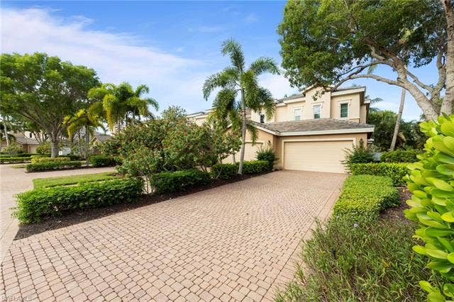 3142 Aviamar Cir, #2104, Naples, FL 34114 Paver driveway, attached garage, mature landscaping, and multi-story stucco exterior