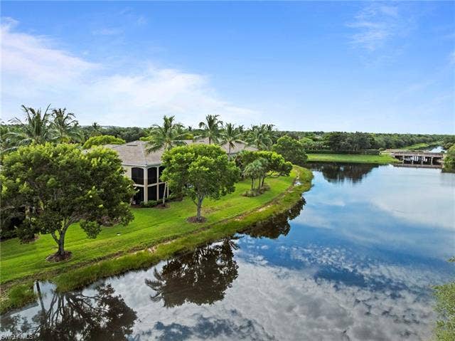 3142 Aviamar Cir, #2104, Naples, FL 34114 Waterfront property featuring a screened balcony, lush landscaping, mature trees, and direct water access