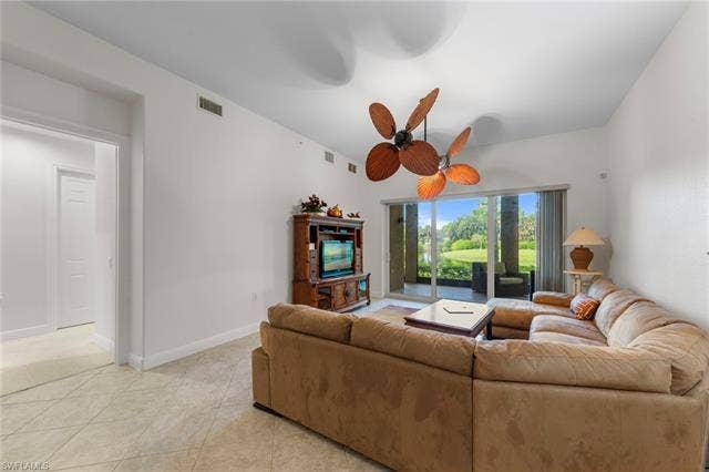 3142 Aviamar Cir, #2104, Naples, FL 34114 Bright, open living room featuring neutral tile flooring, a decorative ceiling fan, large sliding glass doors with natural light, built-in wood cabinetry with integrated entertainment display, and ample seating space with architectural interest