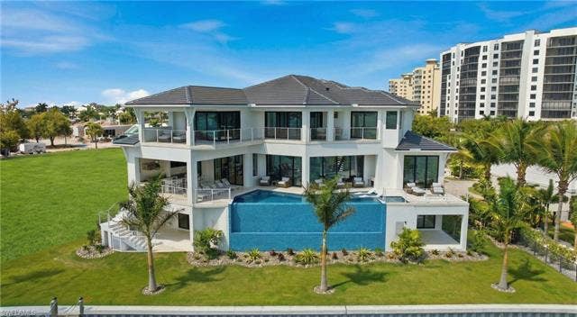 280 Estrellita Dr, Fort Myers Beach, FL 33931 Back of house featuring a balcony, a patio, a yard, and an outdoor pool - Virtually Edited Image